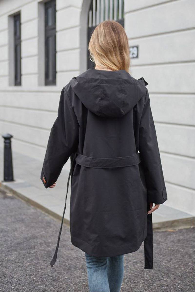 Black water-resistant windbreaker trench jacket with hood and adjustable waist belt worn by woman outdoors