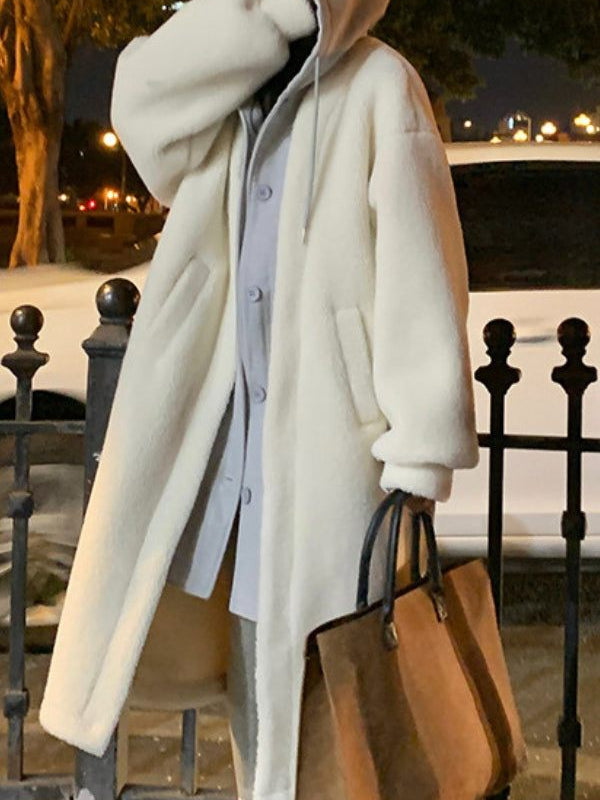 Woman wearing oversized white sherpa long coat with hood carrying brown tote bag at night outdoors