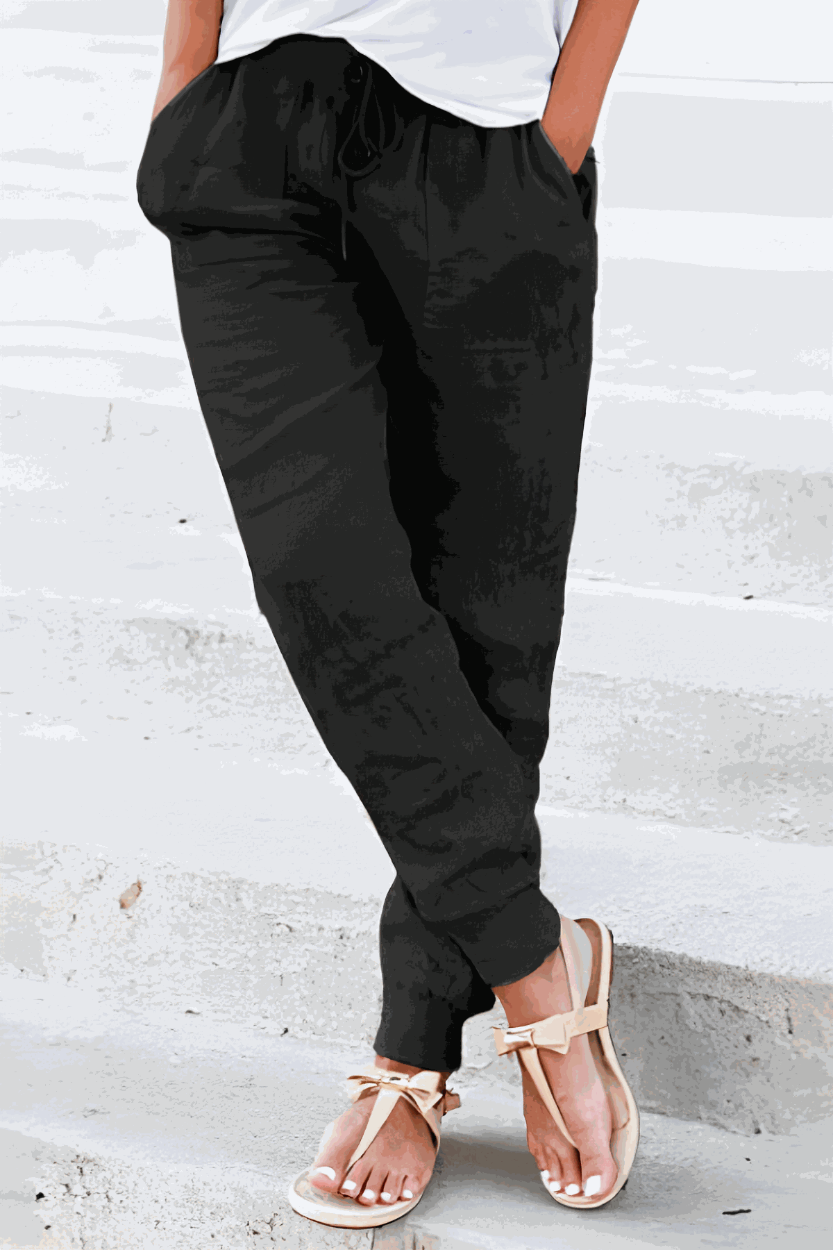 Woman wearing black relaxed chic elastic ankles pants with pockets and white top, standing on concrete steps