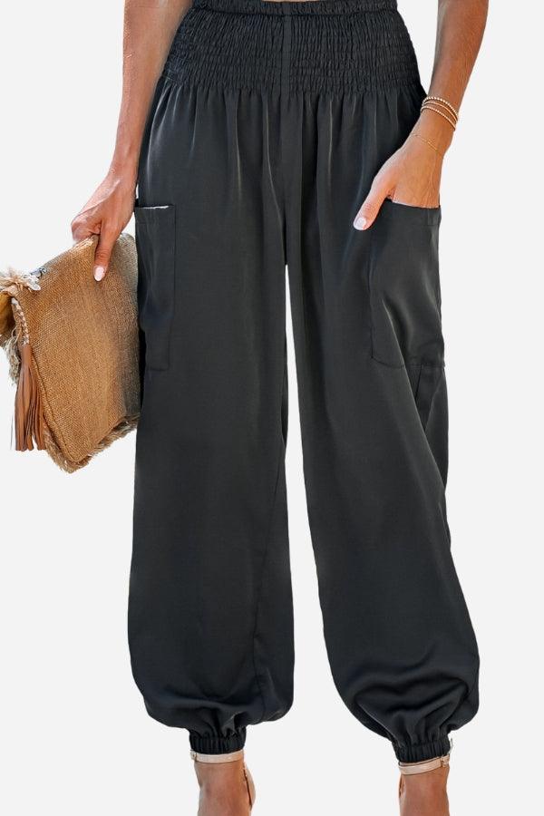 Black Boho Dreamer high-waist elastic pants with pockets and cuffed ankles worn by a model holding a straw clutch bag