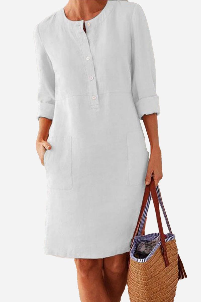 White cotton dress with rolled 3/4 sleeves, half-button front, and pockets, styled with a woven handbag.