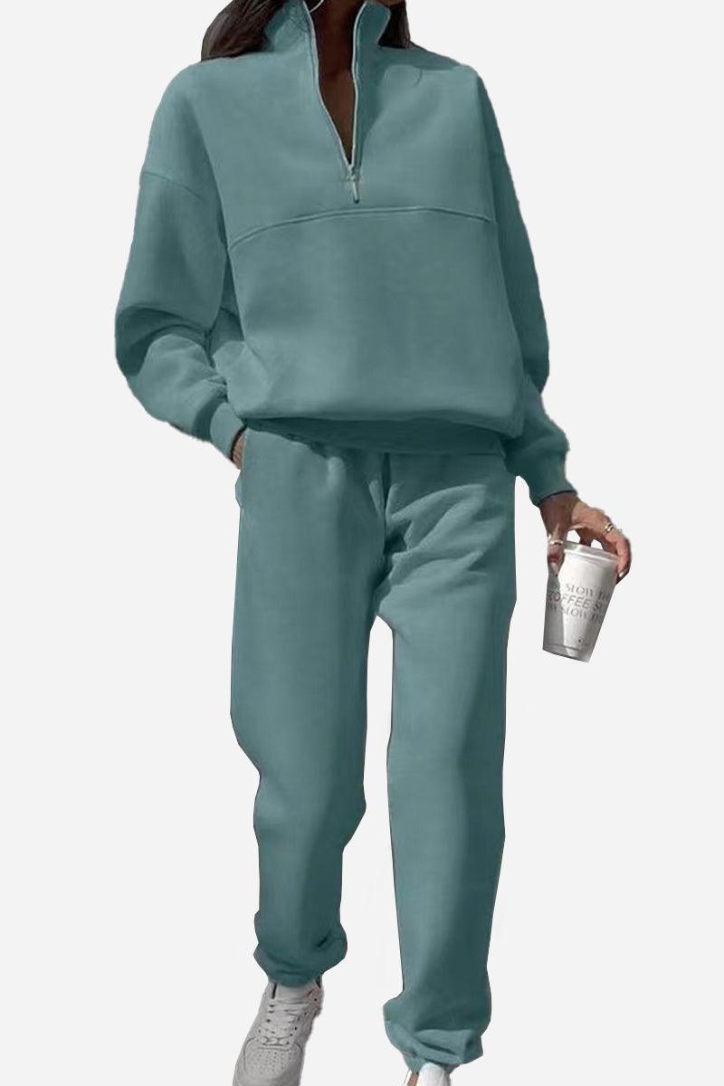Woman wearing teal cotton-blended two-piece tracksuit with high collar and deep zipper, holding a coffee cup
