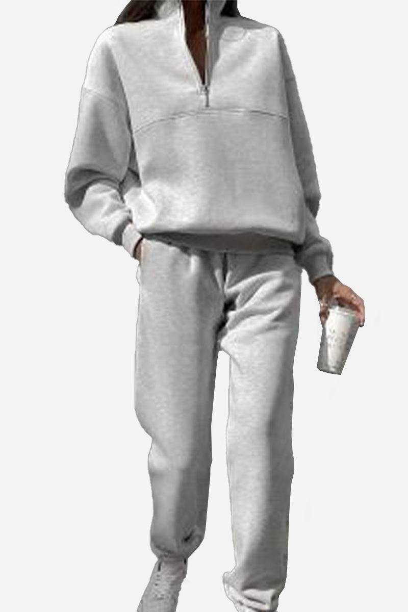 Woman wearing gray cotton-blended two-piece tracksuit with high collar and zipper, holding a cup.
