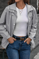 Woman wearing light grey outdoor hooded raincoat and windbreaker with white top and blue jeans