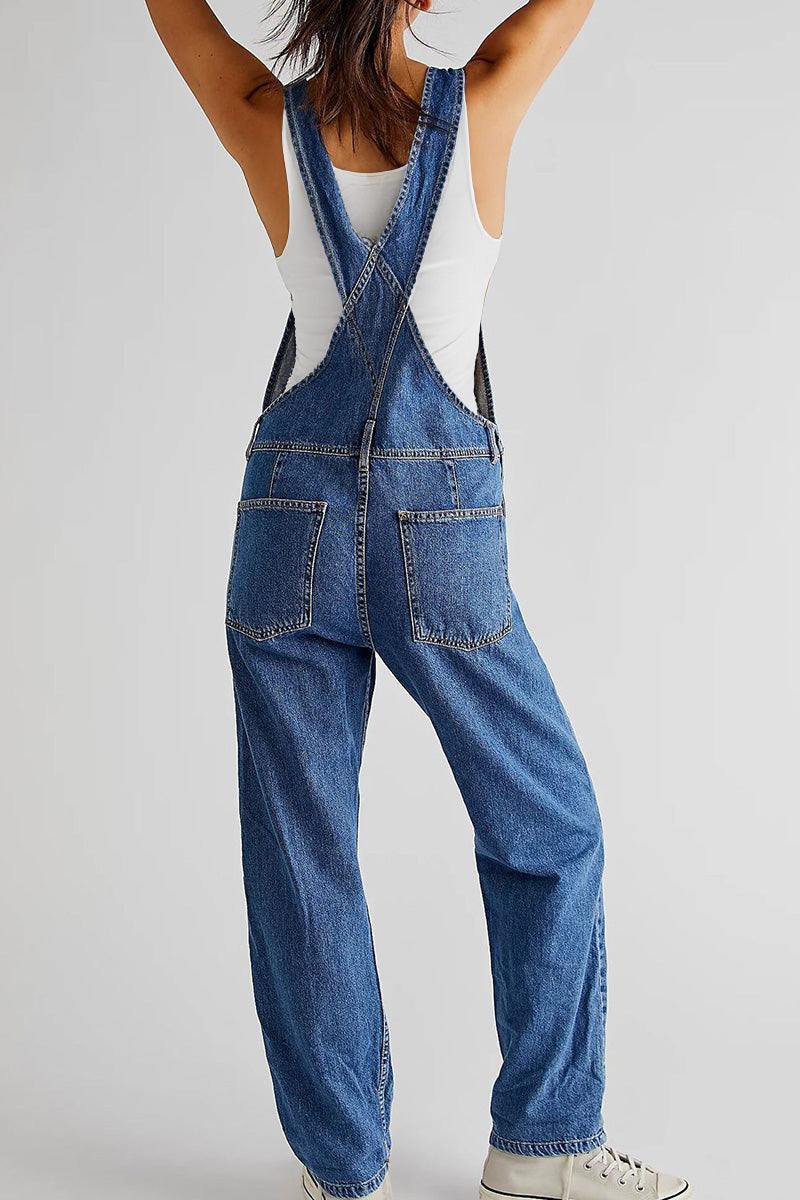 Back view of denim-look tapered-leg adjustable bib overalls worn with a white tank top and sneakers