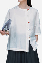 White regenerated cellulose blouse with asymmetrical colorful buttons and oversized fit worn by model holding a fan