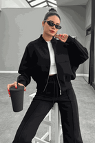 Woman wearing The Voyager Zip Set black zip-front sweatshirt and wide-leg joggers holding a drink cup, styled for travel and casual wear