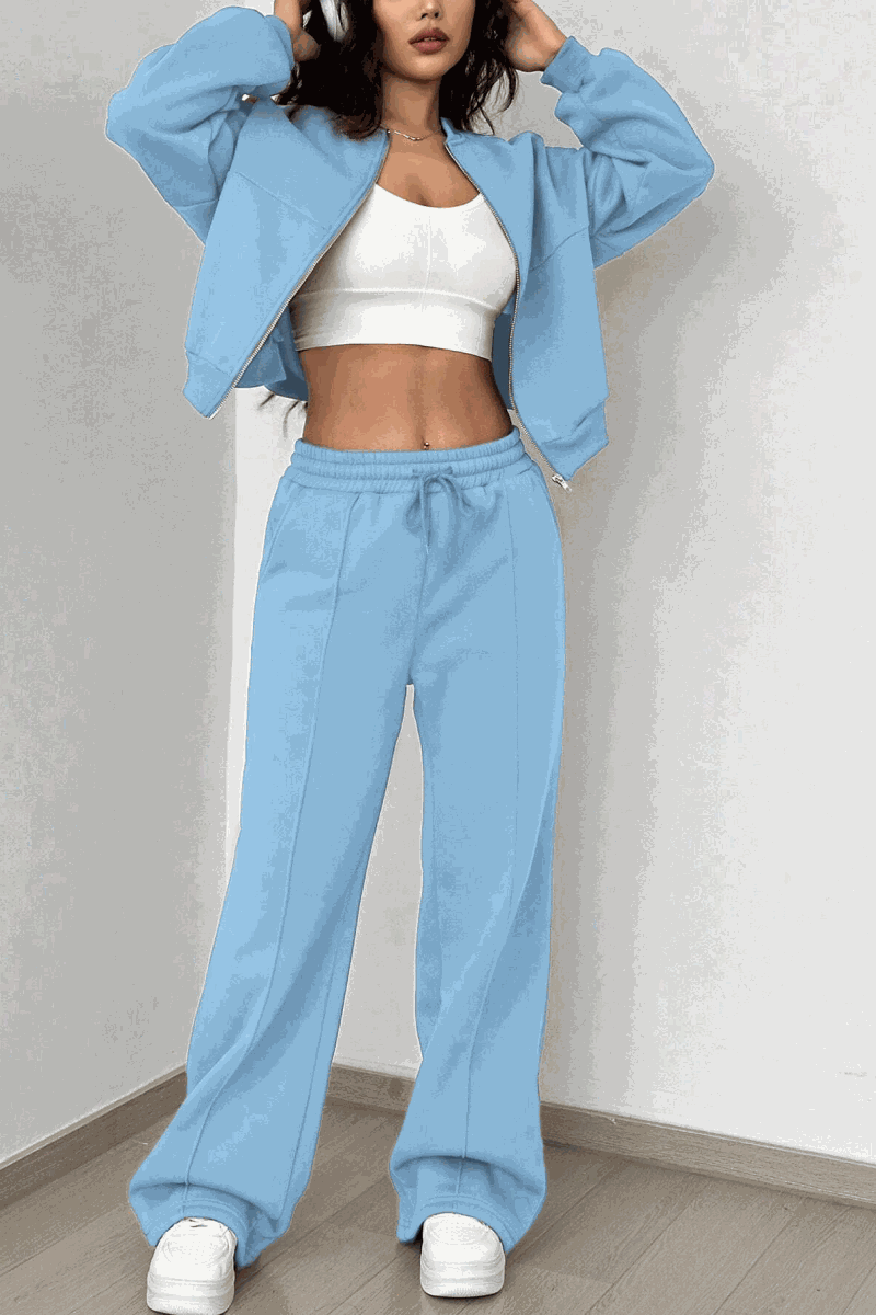 Woman wearing The Voyager Zip Set in light blue with zip-front sweatshirt and wide-leg joggers with pockets, styled with white crop top and sneakers.