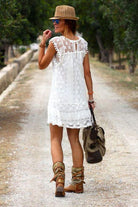 Woman wearing white pom pom lace mini dress with sleeveless design and carrying a bag on a path outdoors
