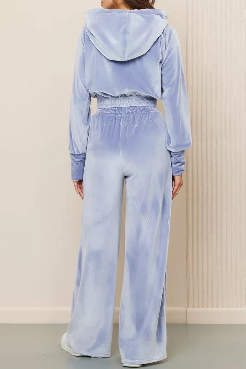 Back view of woman wearing light blue velour tracksuit with cropped hoodie and high-waist pants