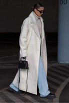 Woman wearing a long white oversized teddy coat with drop shoulders and oversized lapels, paired with light blue jeans and black boots.