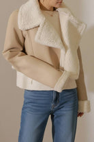 Woman wearing cropped faux leather sherpa jacket with cream shearling collar and cuffs