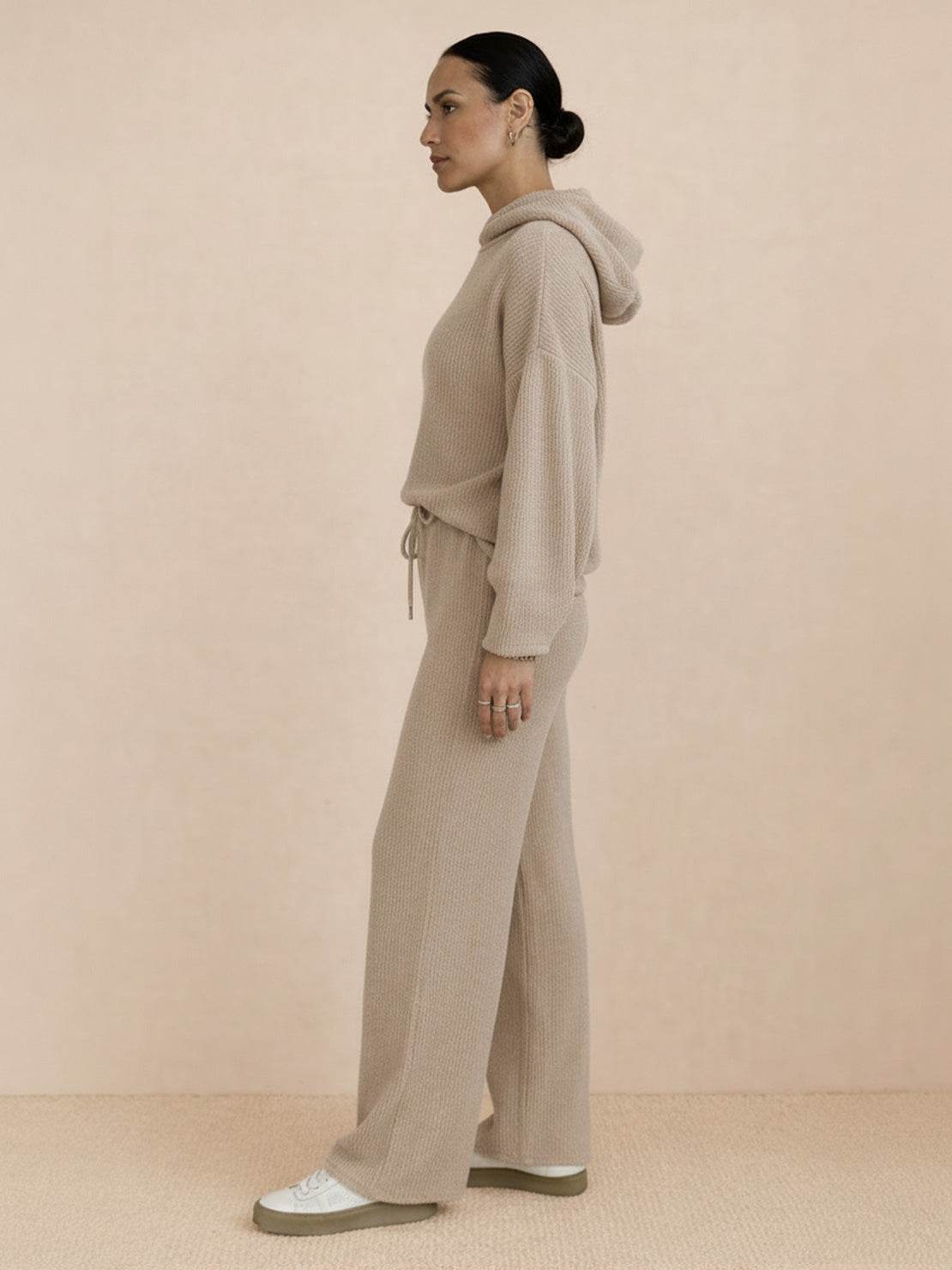 Woman wearing a beige waffle-knit two-piece set with hoodie and wide-leg pants standing sideways