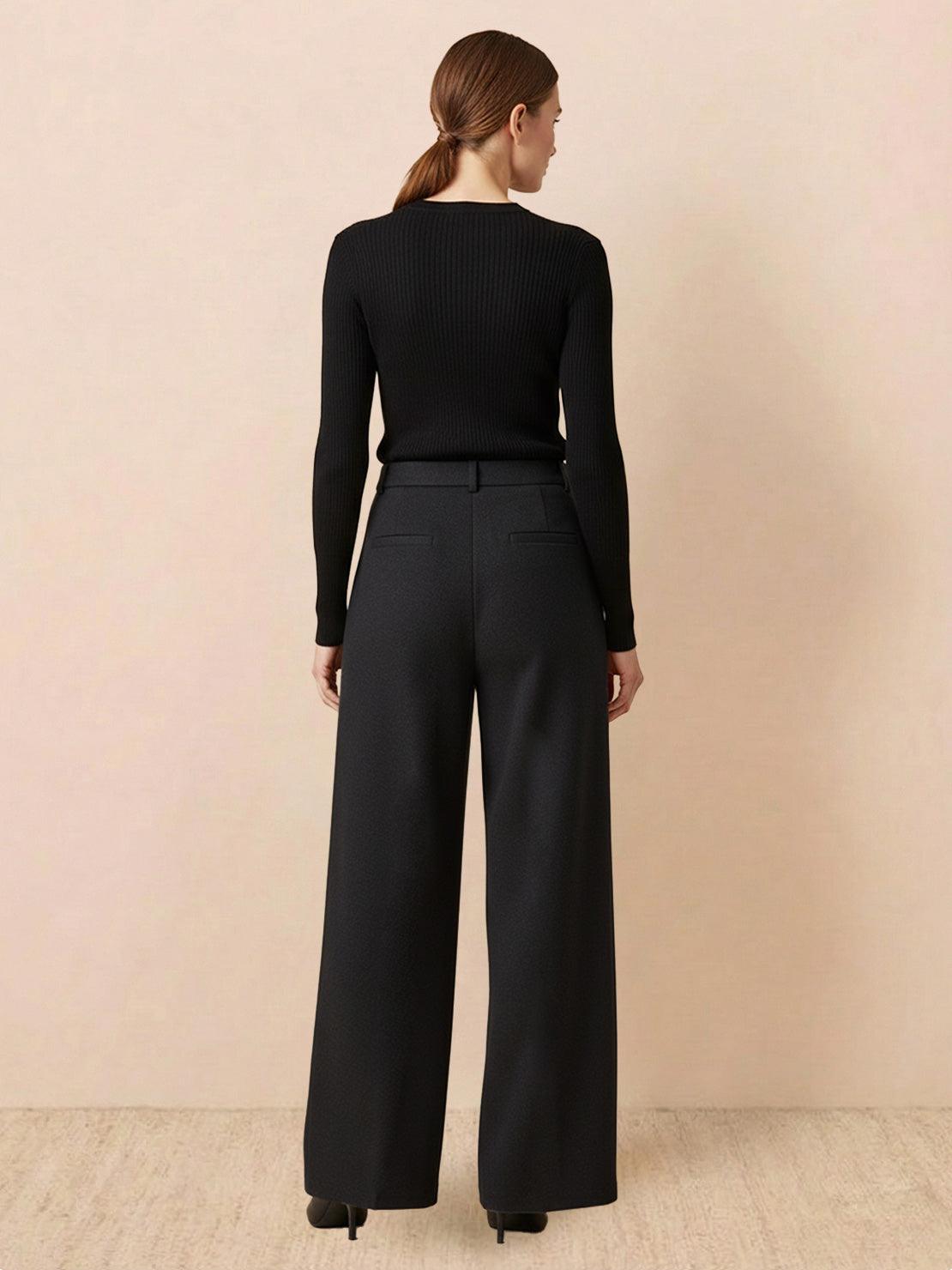 Woman wearing black thermal wool blend trousers with wide-leg fit and elastic back waist standing against a neutral background