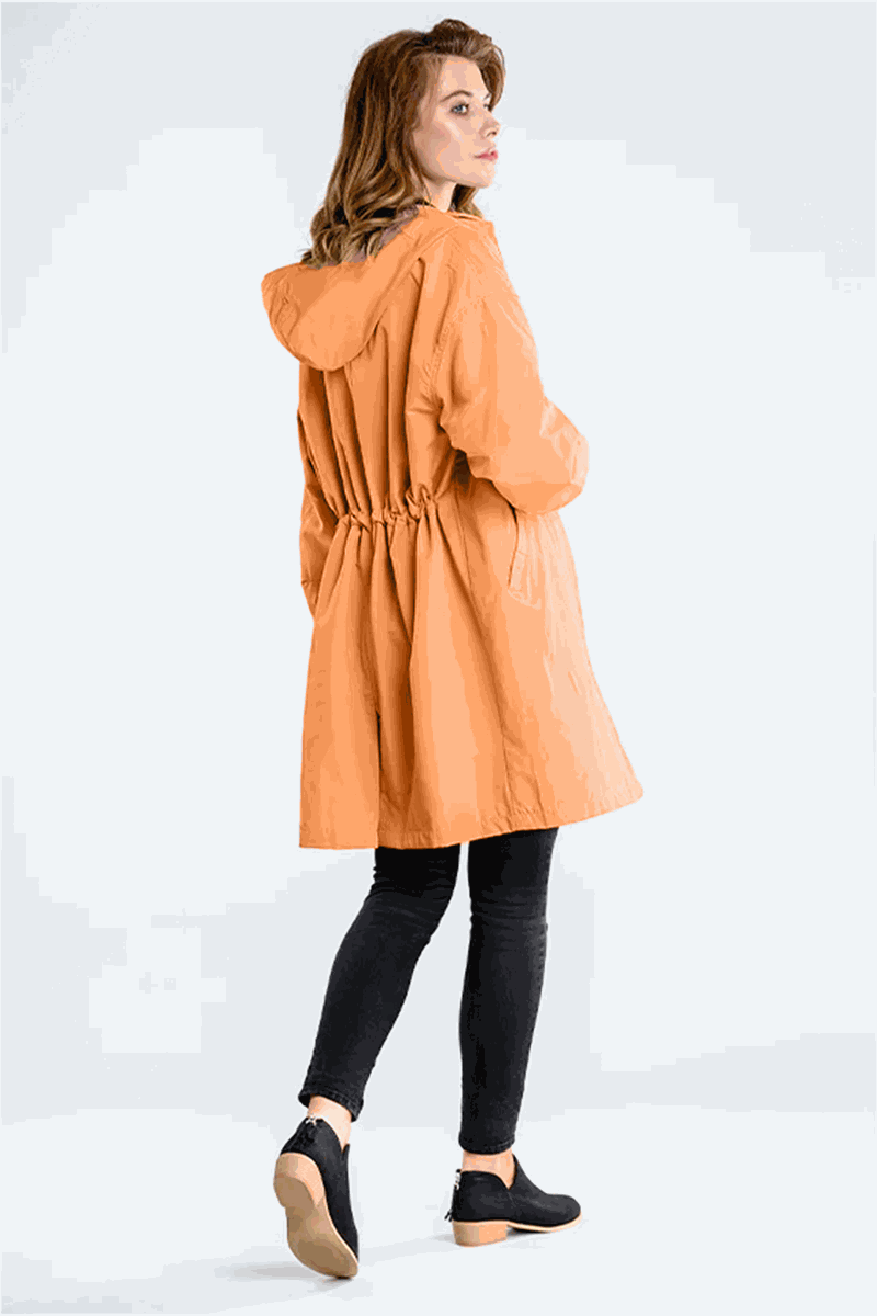 Woman wearing an orange water-resistant oversized hooded windbreaker rain jacket with black leggings and shoes, viewed from the back.