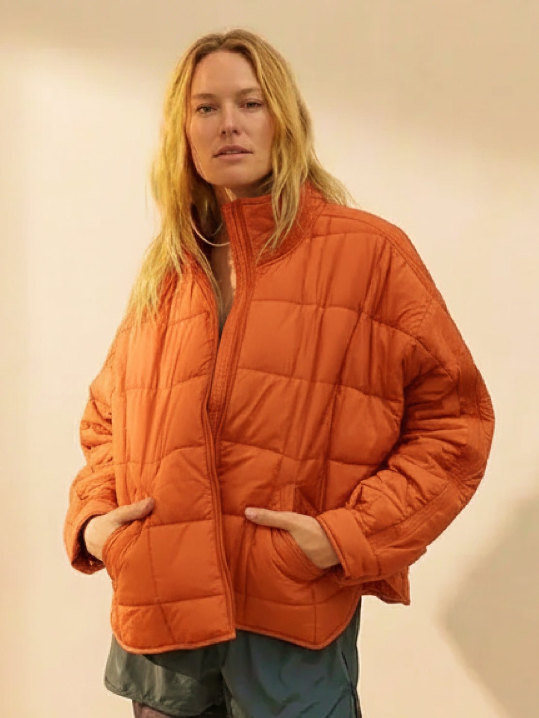 Woman wearing lightweight orange puffer travel jacket with front zipper and pockets