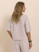 Woman wearing a beige short-sleeved pullover and wide trouser matching set, shown from the back.