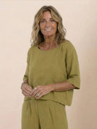 Woman wearing mustard yellow short-sleeved pullover and wide trouser matching set in breathable cotton fabric smiling against beige background