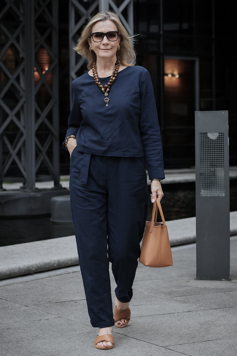 Woman wearing navy cotton-linen monochrome capsule outfit with longline top and wide-leg pants, accessorized with brown handbag and sandals.