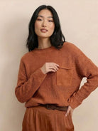 Woman wearing a rust-colored relaxed knit sweater top with pocket and matching trousers embodying European minimalism style