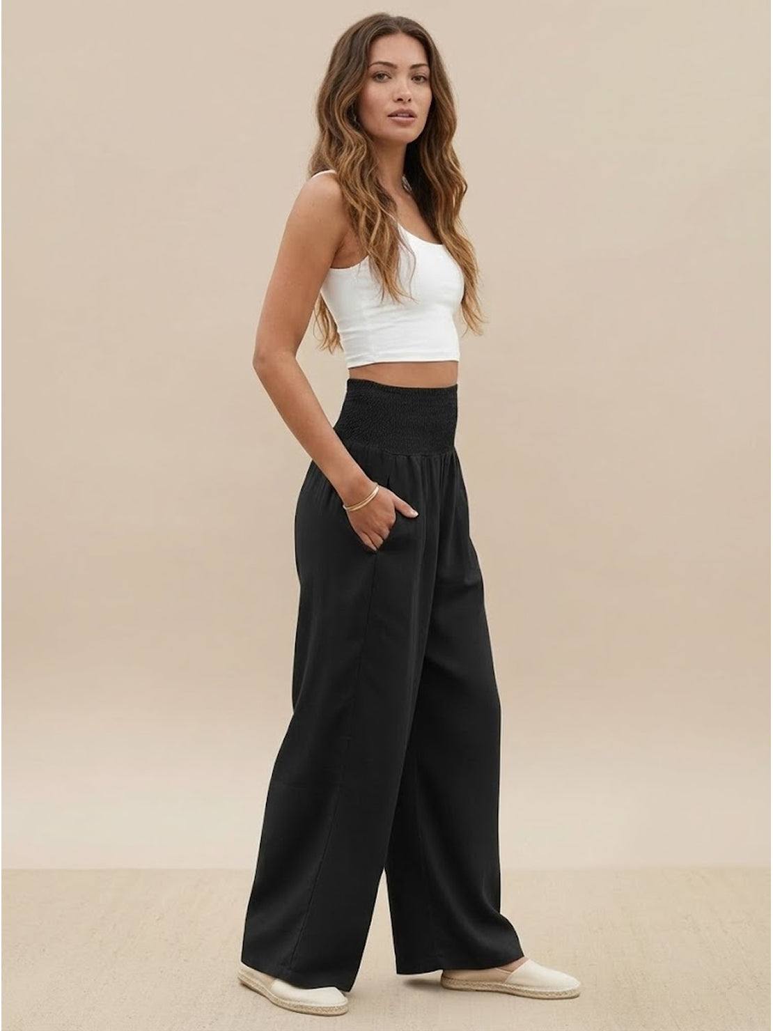 Woman wearing black high-waist cotton linen palazzo pants with wide legs and pockets, styled with a white crop top and casual shoes.