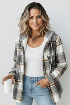 Woman wearing Highland Plaid Shacket with hood, plaid pattern, and fleece lining, styled casually with jeans and white top, holding coffee cup.