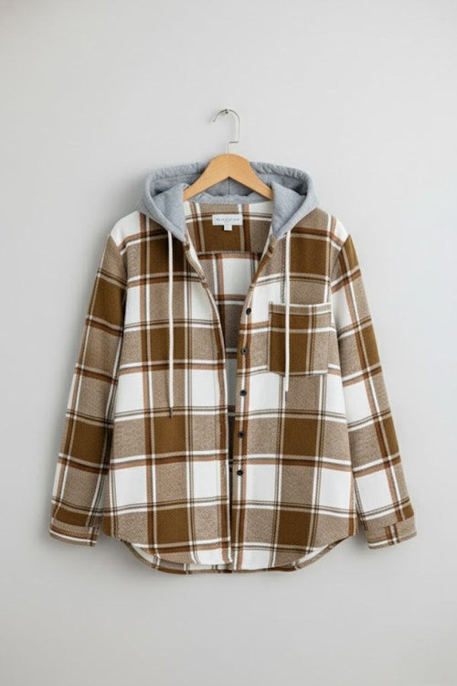 Highland Plaid Shacket with brown and white plaid pattern, soft fleece lining, attached gray hood, button-front, and chest pocket hanging on wooden hanger.