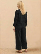 woman wearing loose solid color black two-piece set with long sleeves and wide-leg pants standing back view