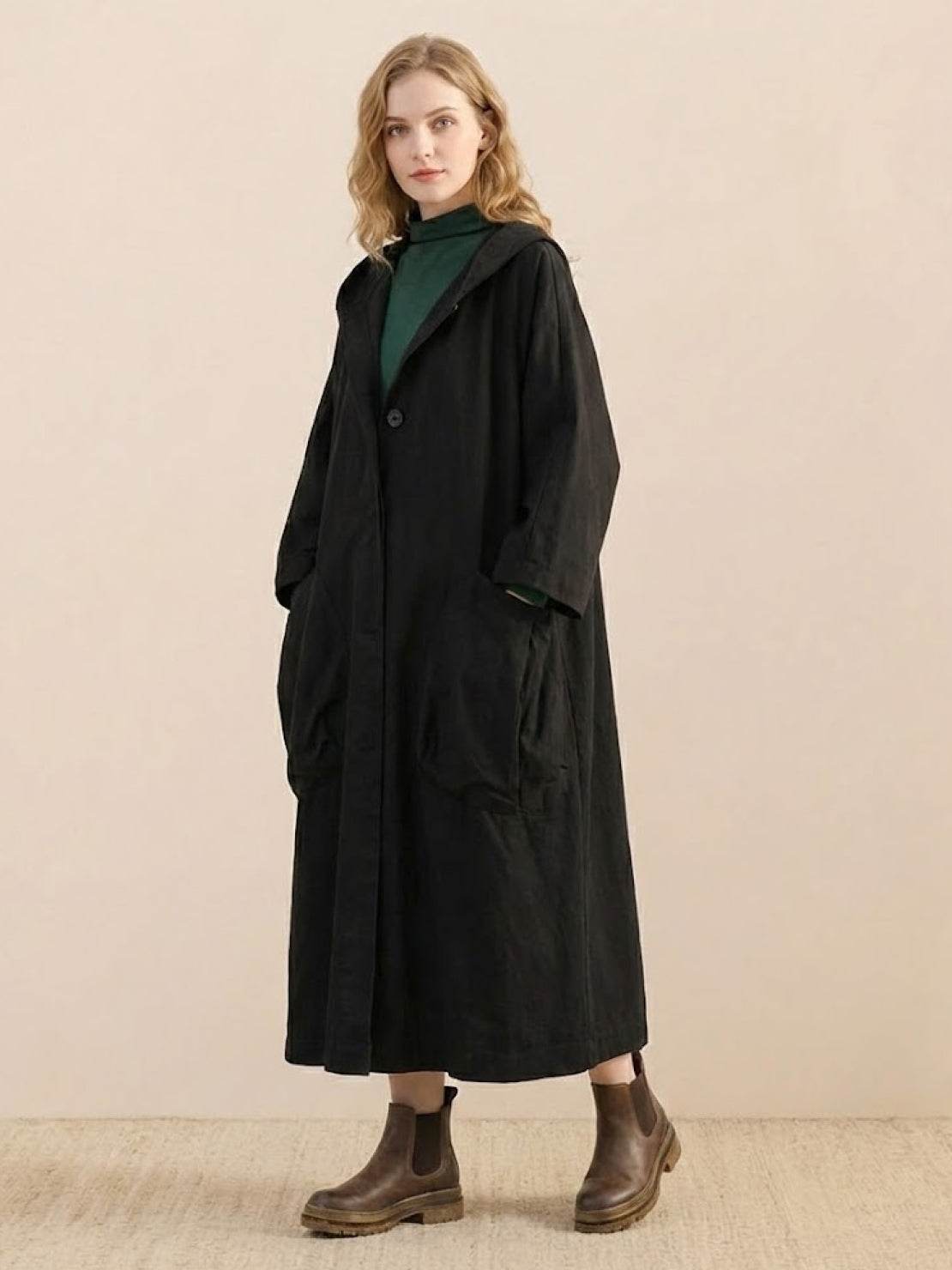 Woman wearing oversized black water-resistant windbreaker jacket with hood and large pockets, styled with boots.