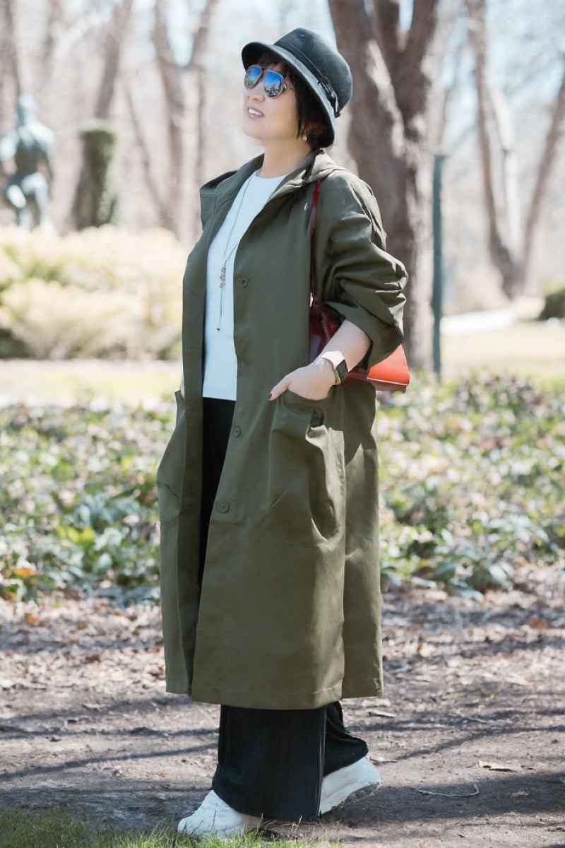 Woman wearing oversized olive green waterproof windbreaker jacket with hood in outdoor setting