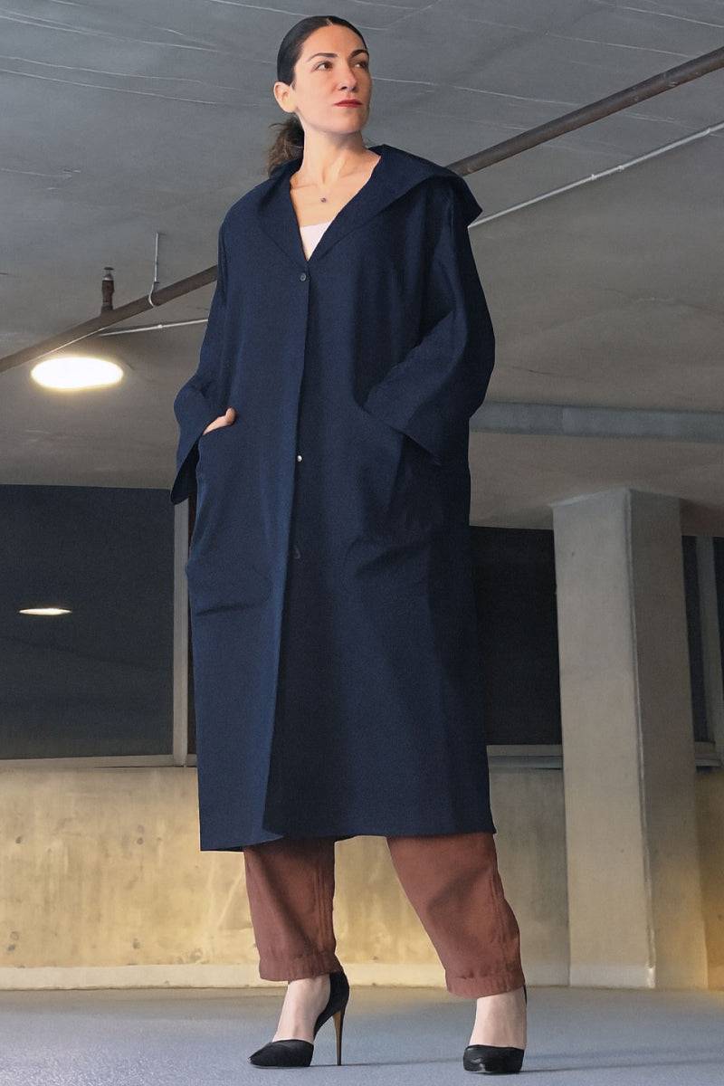 One-size oversized Heritage Windbreaker Jacket in navy with attached hood and large front pockets, worn with brown pants and heels.