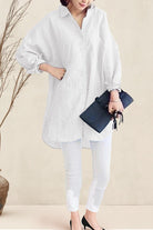Woman wearing oversized white linen shirt with rolled-up sleeves and holding a black clutch bag
