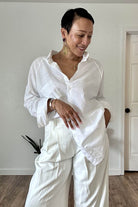 Woman wearing a white oversized linen shirt with relaxed fit and flowing hem paired with white pants indoors
