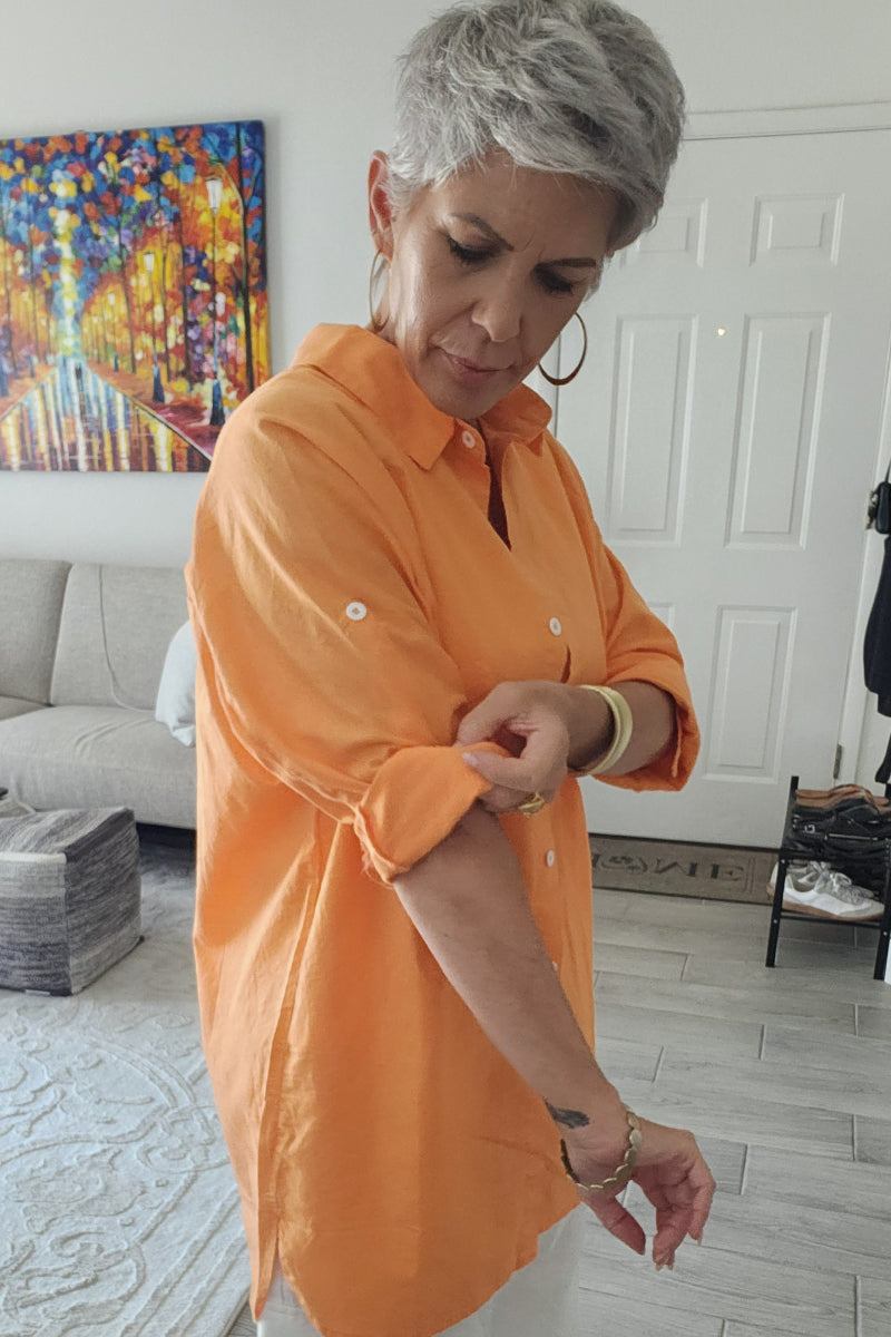 Woman wearing oversized linen shirt in bright orange with rolled-up sleeves indoors