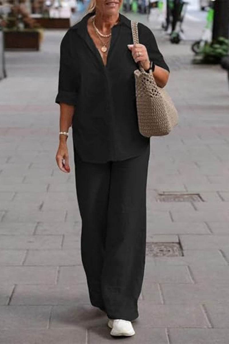 Woman wearing oversized 100% cotton black shirt and wide-leg pants co-ord set walking outdoors with a beige woven shoulder bag and white sneakers.