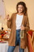 Woman wearing relaxed fit oversized button down knitwear cardigan holding a bottle and cookie in cozy indoor setting