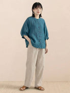 Relaxed loose breathable linen blouse in teal with button-down front and 3/4 sleeves worn with beige pants