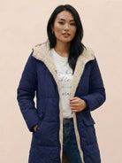Woman wearing navy Sherpa-lined hooded teddy coat with plush interior, durable puffer construction, and front pockets