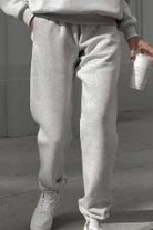 Close-up of light gray cotton blend tracksuit pants worn with white sneakers, casual loungewear style.