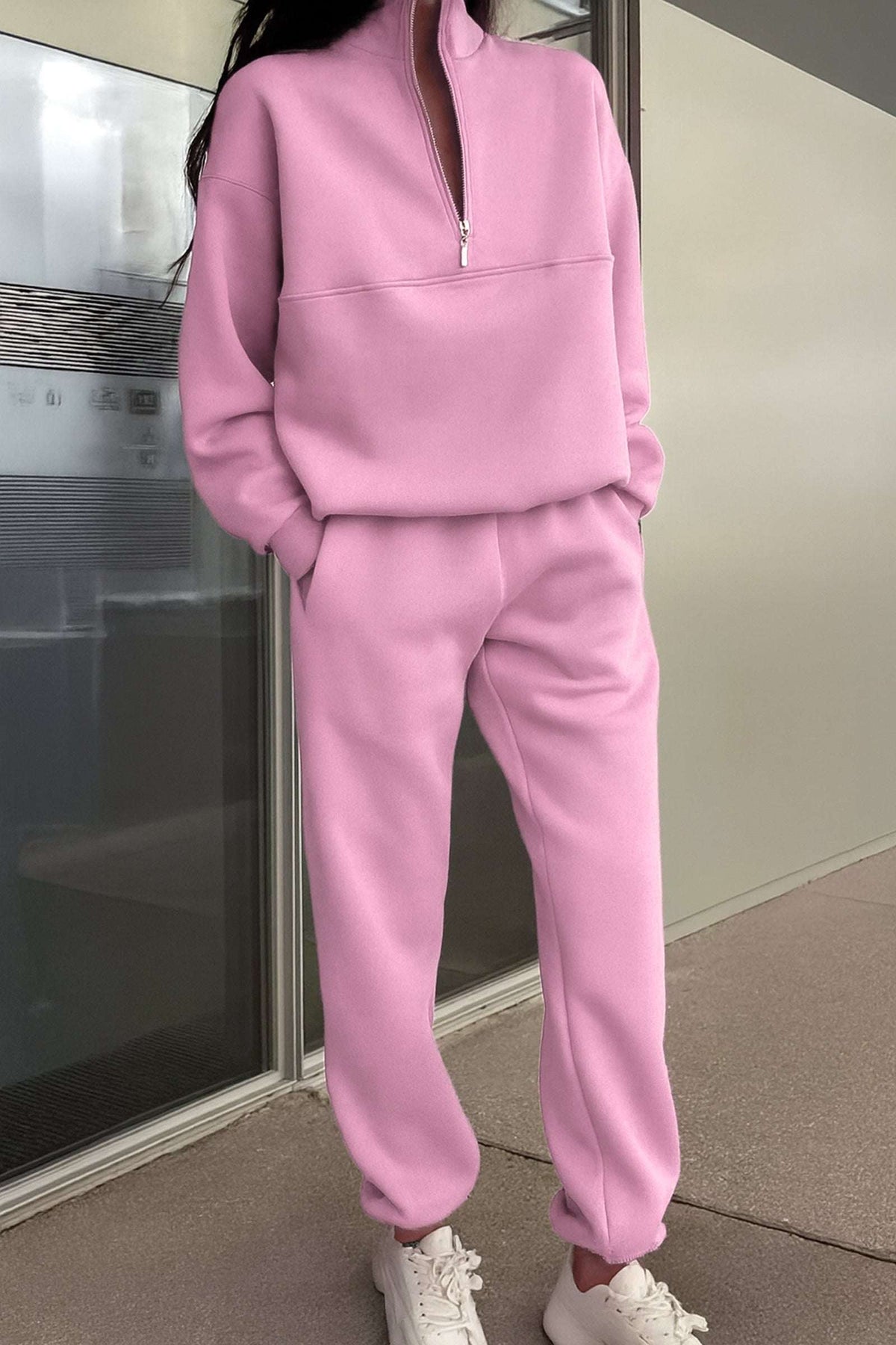 Pink cotton blend tracksuit with zippered high collar and relaxed fit, styled with white sneakers.
