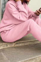 woman wearing soft pink cotton blend tracksuit sitting outdoors using smartphone