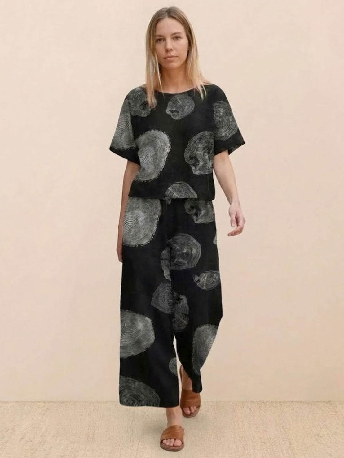 Woman wearing black loose fit co-ord set with wide-leg trousers and short-sleeve top featuring abstract print