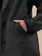 Close-up of black Rain Couture Windbreaker jacket showing water-resistant fabric, button closure, and elastic cuff sleeve on model's arm.