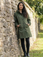 Woman wearing olive green oversized Rain Couture Windbreaker standing by stone wall outdoors